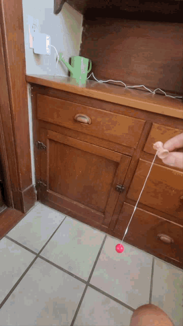 a person playing with a red ball on a string in front of a wooden cabinet