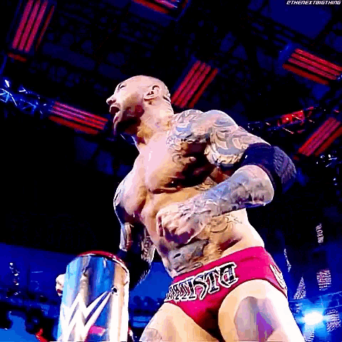 a wrestler with a tattoo on his chest is wearing a pair of red trunks with the word justice on the side