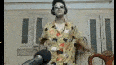 a man in a yellow shirt is standing in front of a microphone .