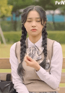 a girl in a school uniform is sitting on a bench eating a candy .