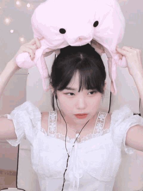 a girl in a white dress is holding a stuffed animal on her head