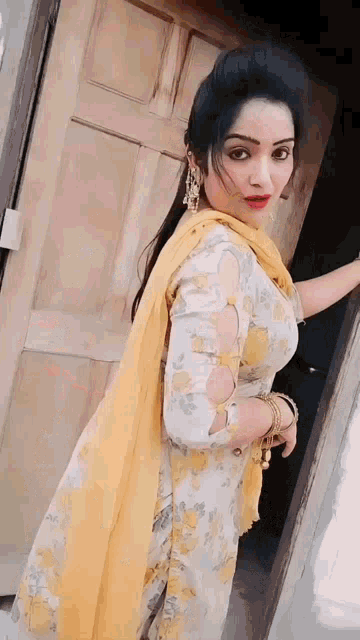 a woman in a yellow and white floral dress is standing in front of a door .