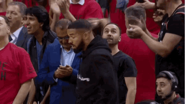 a man in a black hoodie stands in the crowd watching a basketball game