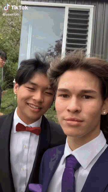 two young men are posing for a picture and one has a red bow tie and the other has a purple tie