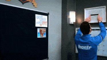 a man in a blue bantr jacket hangs a framed picture on a wall