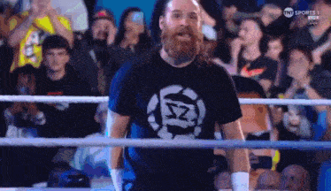 a man with a beard is standing in a boxing ring with a crowd behind him .