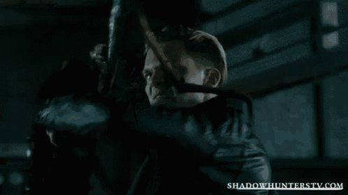 a man holding a sword in a dark room with shadowhunterstv.com written on the bottom right