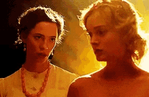 two women are standing next to each other in a dark room . one of the women is wearing a necklace .