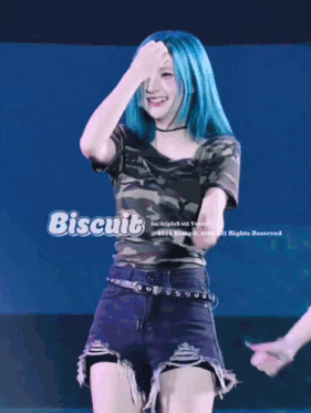 a woman with blue hair is wearing a camouflage shirt and shorts