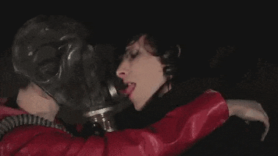 a man wearing a gas mask is kissing a woman in a red jacket .