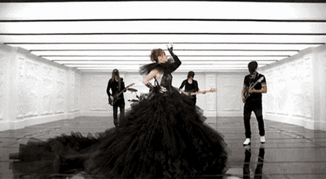 a woman in a long black dress is dancing in front of a band playing guitars