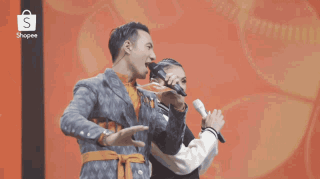 a man speaking into a microphone next to a woman with a shopee logo in the background