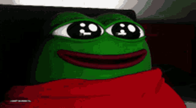 a green frog with big eyes is wearing a red scarf