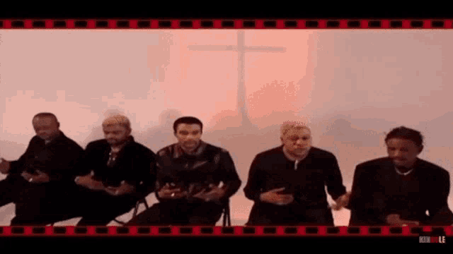 a group of men are sitting in a row in front of a cross .