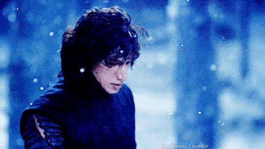 a man in a black sweater is standing in the snow in a forest .