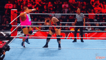 two wrestlers are fighting in a wrestling ring while a referee stands behind them .