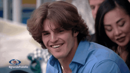 a man in a blue shirt smiles in front of a sign that says grande fratello