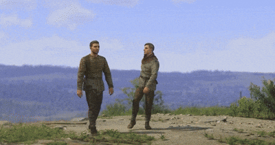two men walking on a dirt road with a view of a body of water in the background