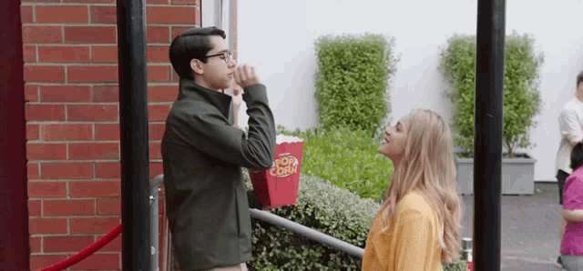 a man and a woman are standing in front of a popcorn bucket