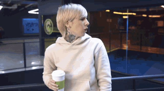 a woman in a white hoodie is holding a green cup