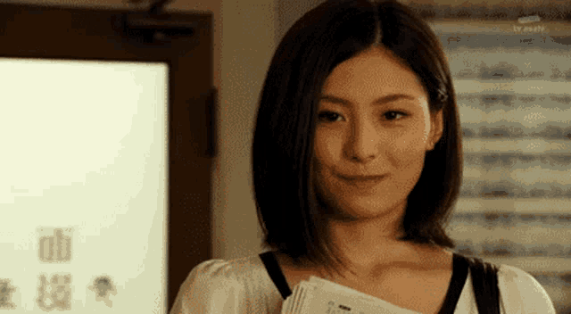 a woman is smiling and holding a stack of papers in front of a door .