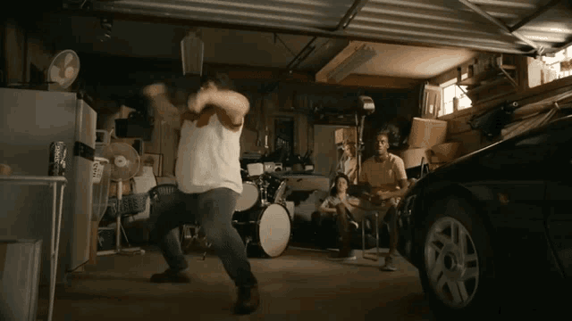 a man in a white shirt is dancing in a garage with a drum set in the background