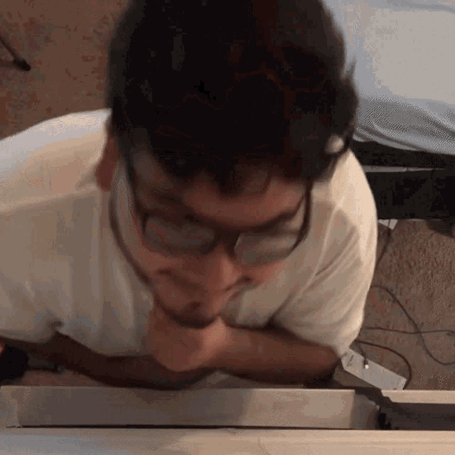 a man wearing glasses and a white shirt is looking down at something