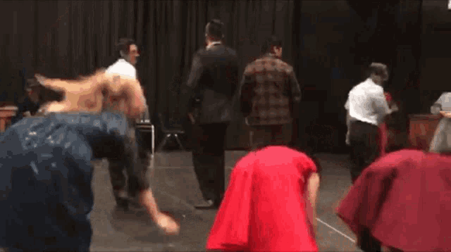 a woman in a red dress is dancing on a stage with other people