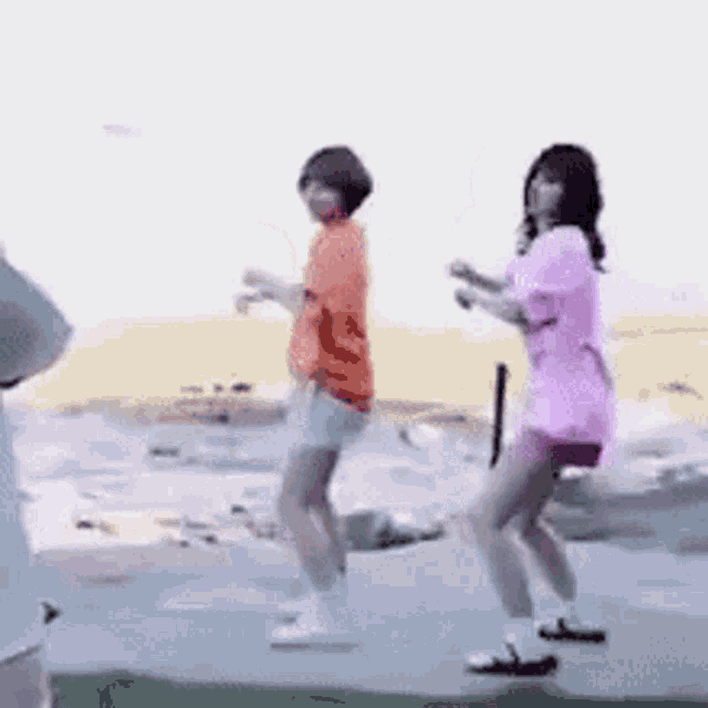 two women are dancing on a sidewalk in front of a body of water .