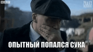 a man in a suit and hat is covering his face with his hand .
