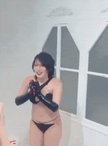 a woman in a black bikini and black gloves is standing in front of a window