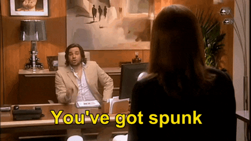 a man in a suit is sitting at a desk talking to a woman who says you 've got spunk .