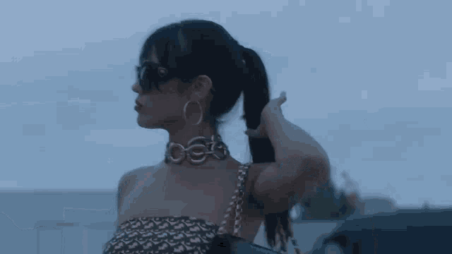 a woman wearing sunglasses , a choker and hoop earrings is standing in front of a car .