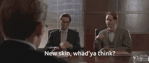 three men in suits and ties are sitting around a table and one of them is saying " new skin whad ya think "
