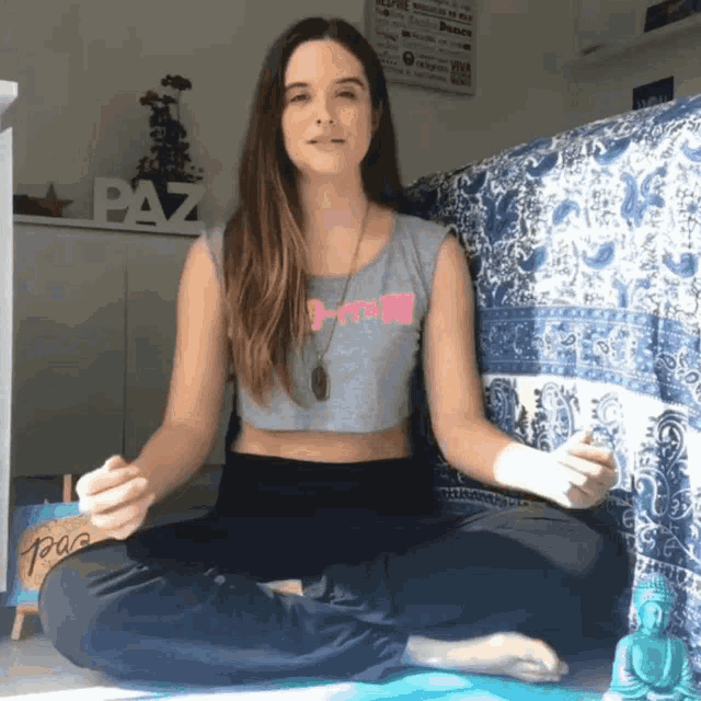 a woman sits in a lotus position with the word paz behind her