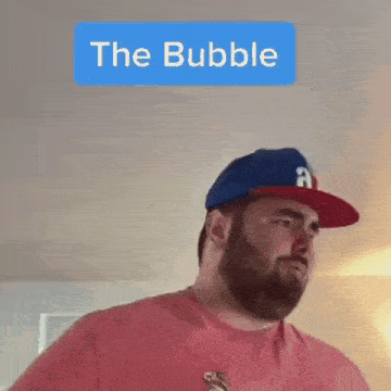 a man with a beard wearing a baseball cap and a red shirt is talking .