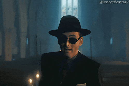 a man wearing a hat and sunglasses is giving the middle finger in a dark room