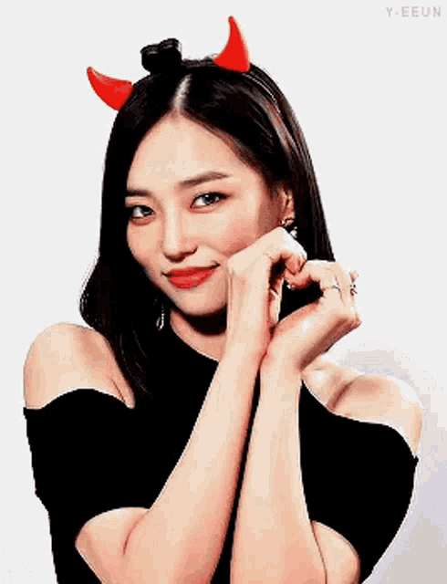 a woman wearing devil horns and a black top is making a heart with her hands .