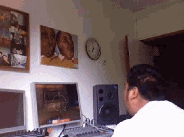 a man sits at a desk in front of two computer monitors and a speaker