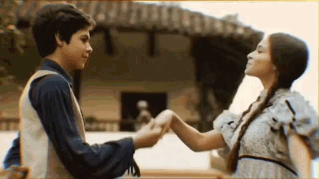 a boy and a girl are holding hands and dancing in front of a building