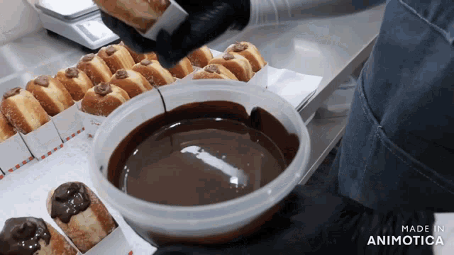 a container of chocolate sauce is being poured over donuts
