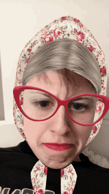 a woman wearing glasses and a floral head scarf makes a face