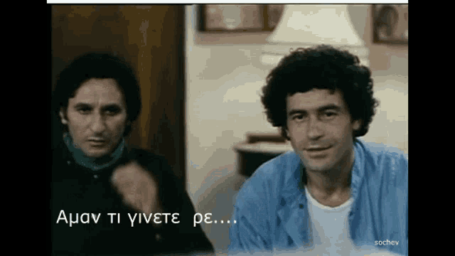 two men are sitting next to each other in a room and one of them is pointing