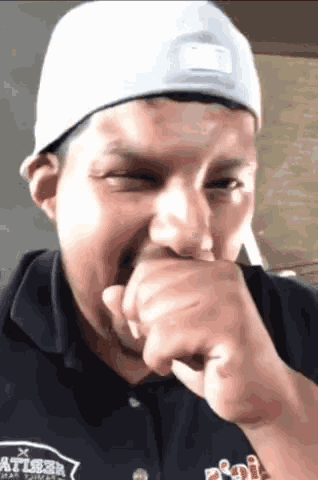 a man wearing a white hat and a black shirt with the word atl on it covering his mouth