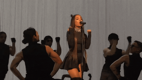 a woman singing into a microphone surrounded by a group of dancers