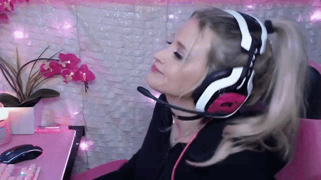 a woman wearing headphones and a microphone is sitting in front of a pink desk