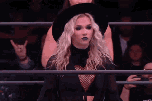 a woman wearing a black hat and black lipstick stands in a ring