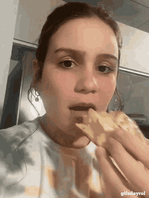 a close up of a woman eating a slice of pizza with gifsdayrol in the bottom right corner