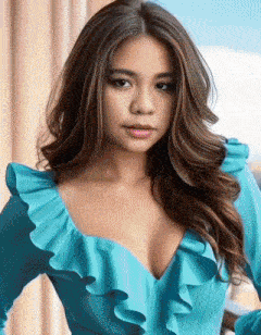 a woman in a blue dress with ruffles on the sleeves is looking at the camera