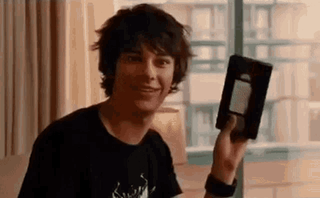 a young man in a black shirt is holding a vhs tape in his hand .